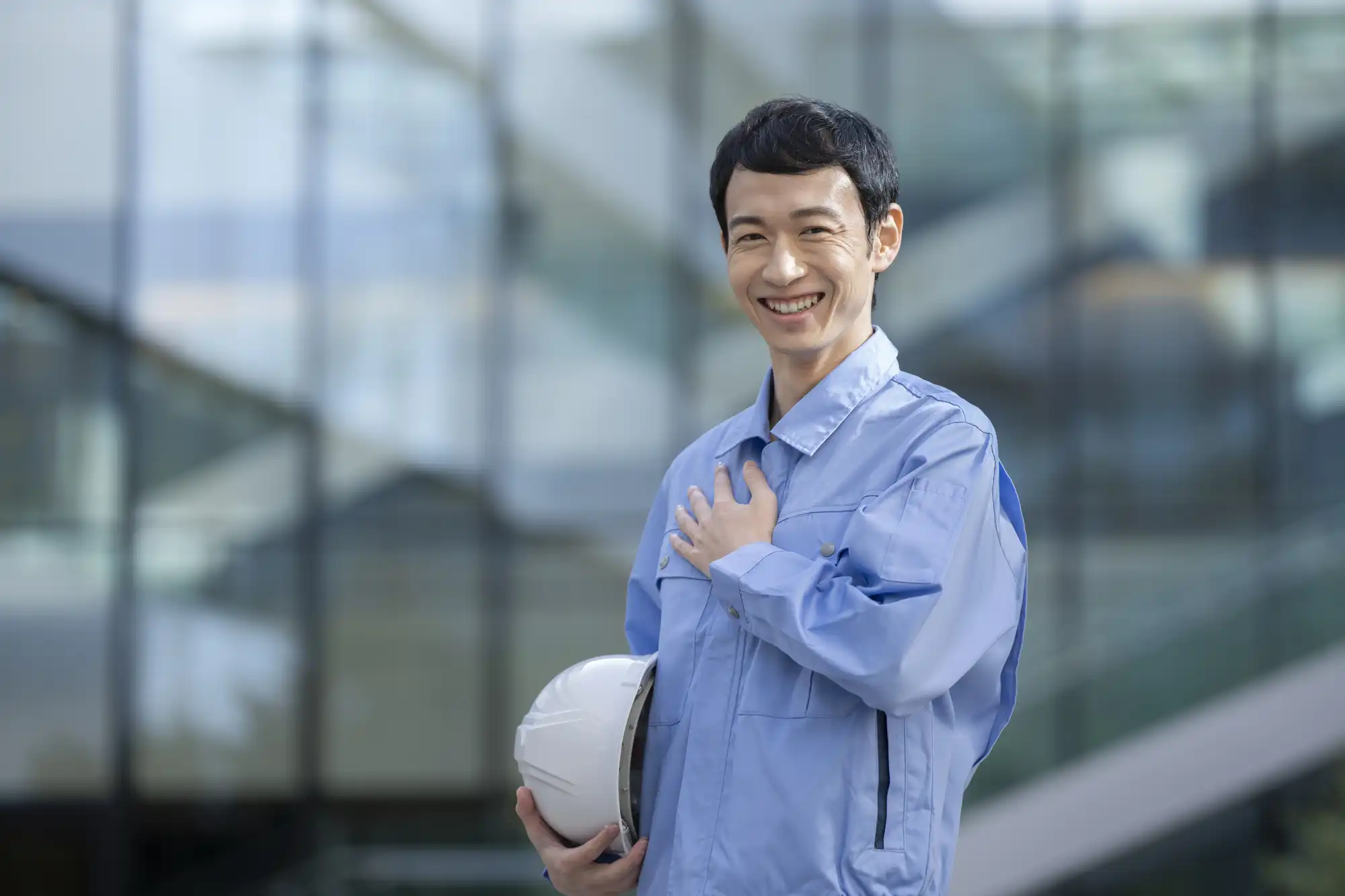 ヘルメットを持った青い作業服の男性